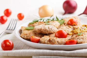 Fried pork chops with tomatoes and herbs on a white ceramic plate on a white wooden background. side view, close up.