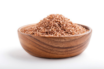 Wooden bowl with unpolished brown rice isolated on white background. Side view.