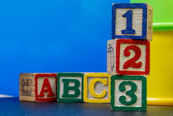 six wooden and colored play blocks, a,b,c, one, two, three. blue background. Learning beginnings...