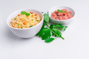 Canned tuna and delicious homemade couscous with dates, raisins, parsley, tomato, lemon and olive oil in a white bowl on white background, copy space, studio shot, soft light