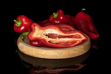 Group of three whole one half of sweet red bell pepper on bamboo plate isolated on black glass
