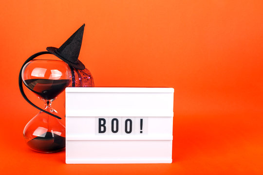 Halloween themed cinema light box on the bright orange background with funny witch hat and black sand hourglass