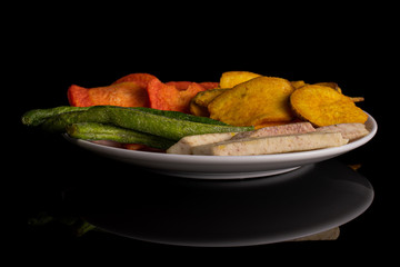 Lot of whole dry vegetable chip on white ceramic plate isolated on black glass