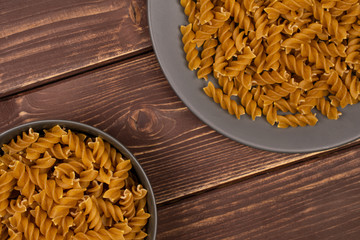 Lot of whole dry brown wholegrain fusilli on gray ceramic plate in gray ceramic bowl flatlay on brown wood