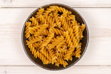 Lot of whole dry brown wholegrain fusilli in dark ceramic bowl flatlay on white wood