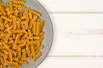 Lot of whole dry brown wholegrain fusilli on gray ceramic plate flatlay on white wood