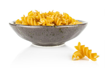 Lot of whole dry brown wholegrain fusilli two are aside and the rest is in dark ceramic bowl isolated on white background