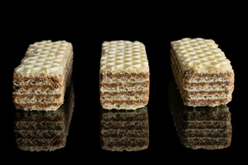 Group of three whole crispy beige hazelnut wafer cookie in row isolated on black glass