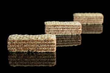 Group of three whole crispy beige hazelnut wafer cookie placed diagonally isolated on black glass