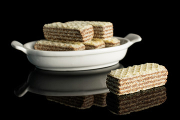 Group of six whole crispy beige hazelnut wafer cookie in white oval ceramic bowl isolated on black glass
