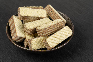 Lot of whole crispy beige hazelnut wafer cookie in dark ceramic bowl on grey stone
