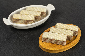 Group of six whole crispy beige hazelnut wafer cookie in white oval ceramic bowl on bamboo coaster on grey stone