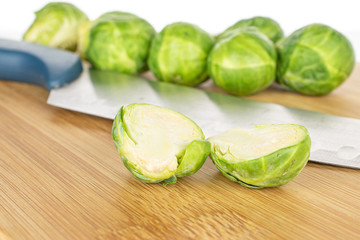 Group of six whole two halves of fresh green brussels sprout on bamboo cutting board with steel knife isolated on white background