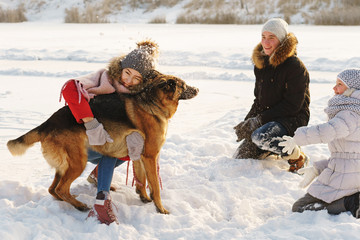 Fototapeta na wymiar Joyful teens spend time together with lovely pet German Shepherd Dog on a walk in the winter park on a sunny day. Having fun playing in snow outdoors. Time for cheery. Happy family. Playful mood
