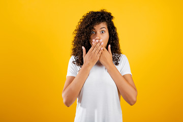 surprised black woman covering her mouth isolated over yellow