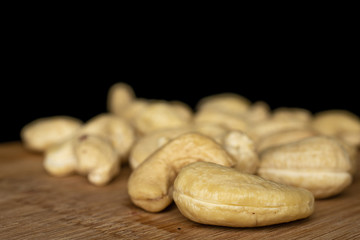 Lot of whole brown nut cashew closeup on bamboo cutting board isolated on black glass