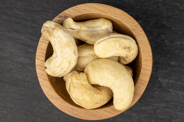 Lot of whole brown nut cashew in bamboo bowl flatlay on grey stone