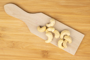 Group of nine whole brown nut cashew on wooden cutting board flatlay on light wood