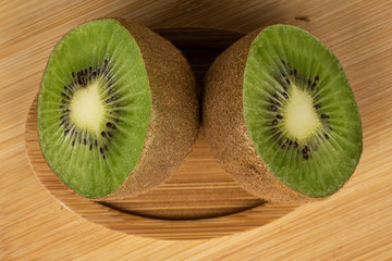 Group of two halves of exotic brown kiwi on round bamboo coaster flatlay on light wood