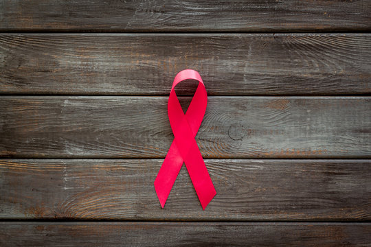 Pink ribbon as symbol of breast cancer awareness on dark wooden background top view copy space