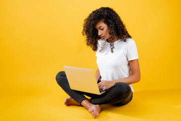 Naklejka premium happy african black woman sitting with laptop isolated over yellow