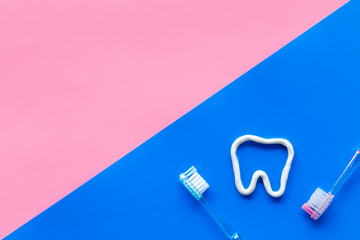 Teeth brushing concept. Tooth drawn with toothpaste near toothbrushes on pink and blue background top view