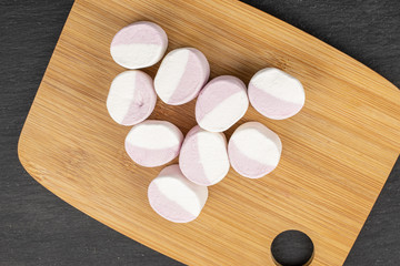 Fototapeta na wymiar Group of nine whole sweet pastel marshmallow on bamboo cutting board flatlay on grey stone