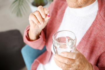 Elderly woman taking medicine at home, closeup