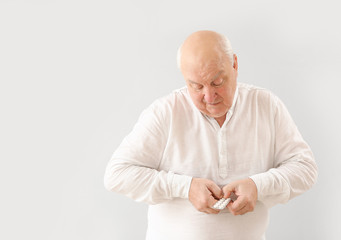 Elderly man with pills on light background