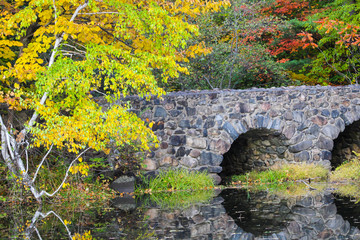 Stone bridge, maple forest in autumn, and reflections on lake, St-Bruno, Quebec, Canada