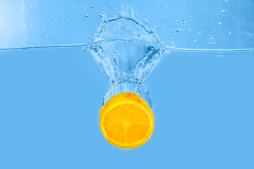 Falling of orange piece into water on light background