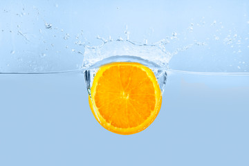 Fototapeta na wymiar Falling of orange piece into water on light background
