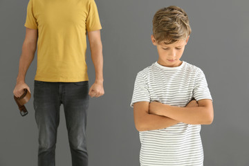 Man threatening his little son against grey background. Physical punishment concept