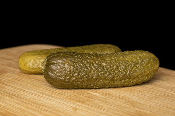 Group of two whole sour green pickle front focus on bamboo cutting board isolated on black glass