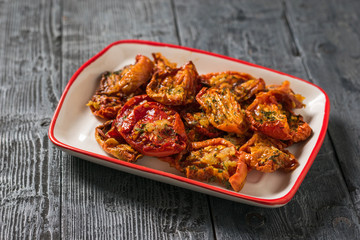 Dried tomatoes with garlic and pepper in olive oil in a plate on a wooden table. Vegetarian food.