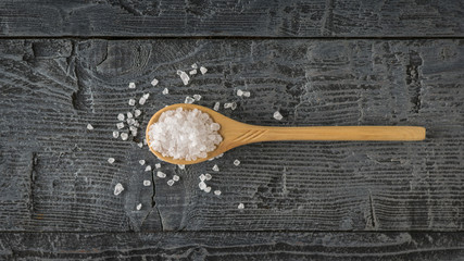 Spoon of light wood filled with large sea salt on a wooden table. The view from the top.