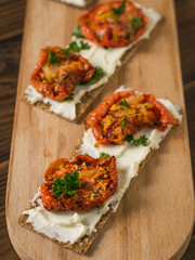 Two bread toast on a chopping Board with cream cheese and sun-dried tomatoes on a wooden table.