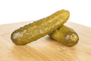 Group of two whole sour green pickle on bamboo cutting board isolated on white background
