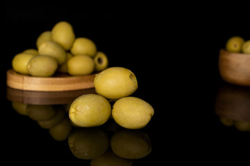 Lot of whole marinated green olive in bamboo bowl on round bamboo coaster isolated on black glass