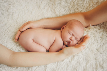 naked newborn baby lying on the hands of parents on a white background. Imitation of a baby in the womb. beautiful little girl sleeping lying on her stomach.