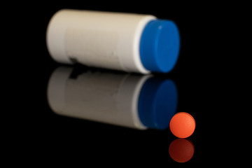 One whole orange tablet pharmacy with plastic bottle isolated on black glass