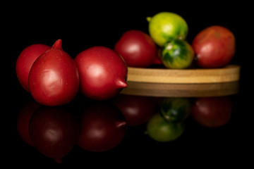 Group of seven whole fresh tomato de barao on round bamboo coaster isolated on black glass