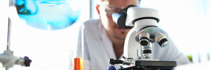Portrait of a young chemist looking in binocular