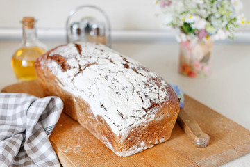 Loaf of bread, jar with honey and summer flowers on the table.