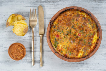 Ceramic bowl with vegetable frittata, simple vegetarian food. Frittata with tomato, pepper, onion and cheese on wooden table, close up. Italian egg omelette