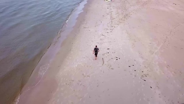 Aerial Shot of Man Walking On Sandy Beach on a Cloudy Day. Beach Walk Slowmotion. Man Walking on a Beach Slowmotion,