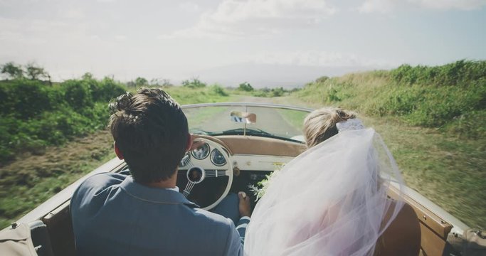 Happy newly wed couple eloping on a country road in a classic convertible, multi ethnic luxurious couple having a fun drive on a country road