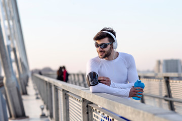 Man with heaphones resting before jogging and listen music with bottle of water on hand