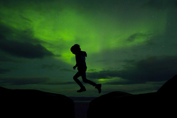 Sillhouette of preschool child, jumping over gap on aurora borealis sky background