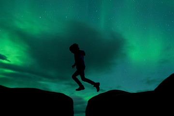 Sillhouette of preschool child, jumping over gap on aurora borealis sky background
